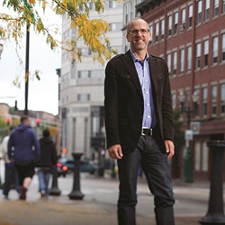 man standing on sidewalk of city smiling at camera