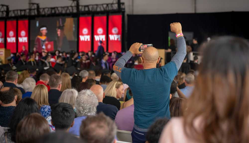 A family member takes a photo of a graduate while raising a fist in the air.