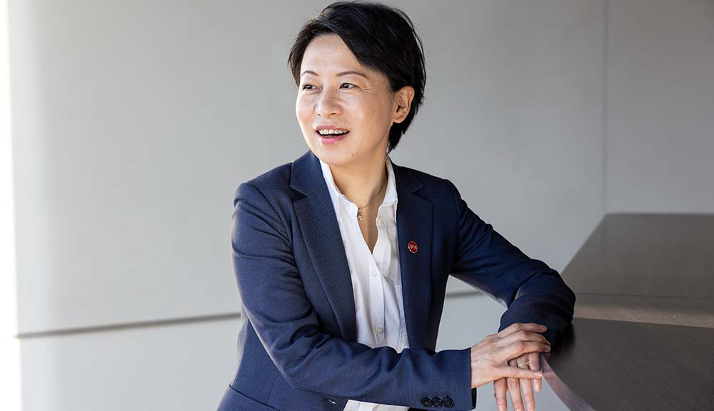 Grace Wang smiles while looking off-camera against a gray background.