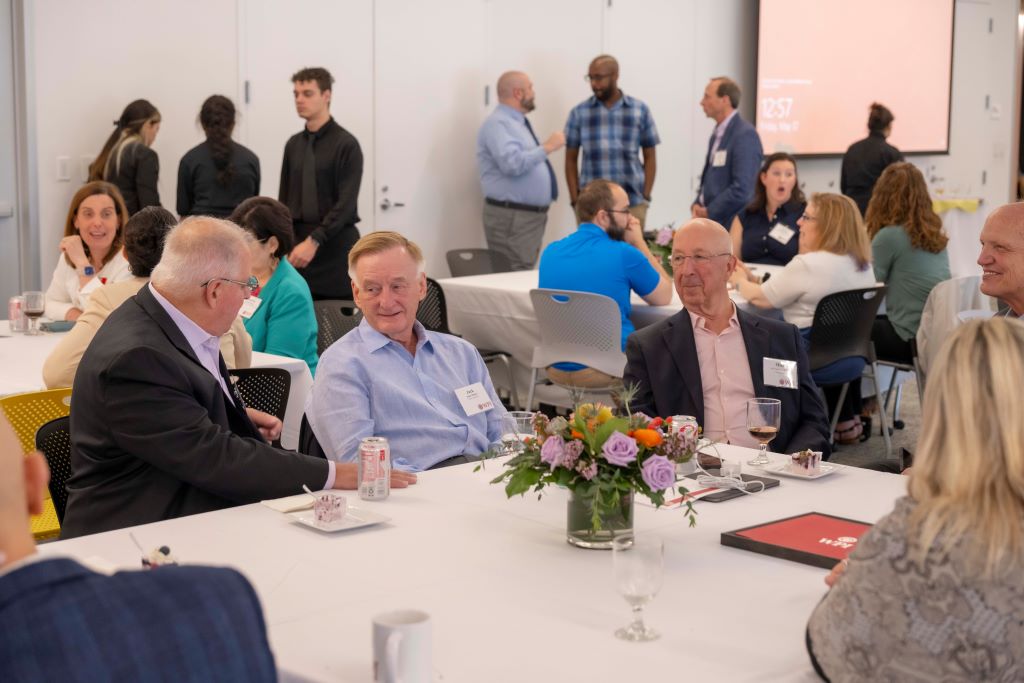 A table of men chatting with people standing in the background at the Board of Trustees Outstanding Staff Awards luncheon