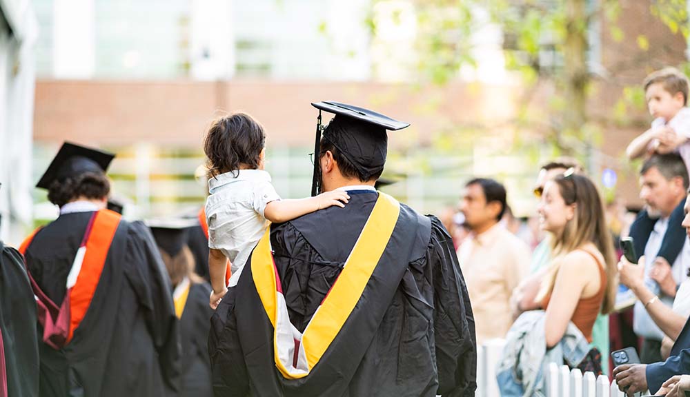 A graduating MS student carries a small child after the graduate commencement ceremony.