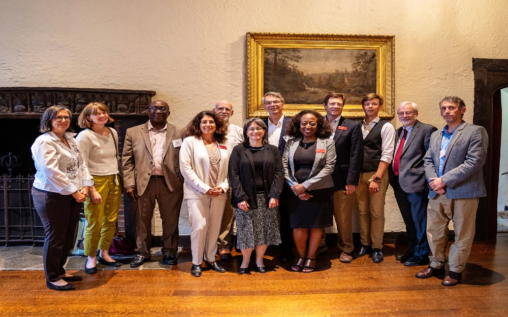 a group of people standing in front of a fireplace with a painting hanging above it