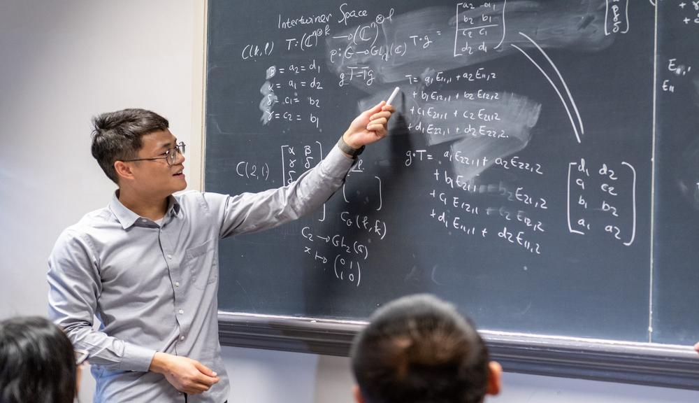 a male in a white shirt at a blackboard of math problems