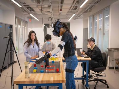 students working over a table with one student in AI headgear