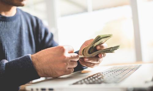man at computer holding money