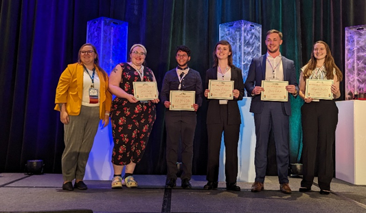 Sara Frunzi accepting her People’s Choice Award for her poster, along with the other poster awardees and Abby Ray (she/they), the oSTEM Vice President of Marketing and Communications.