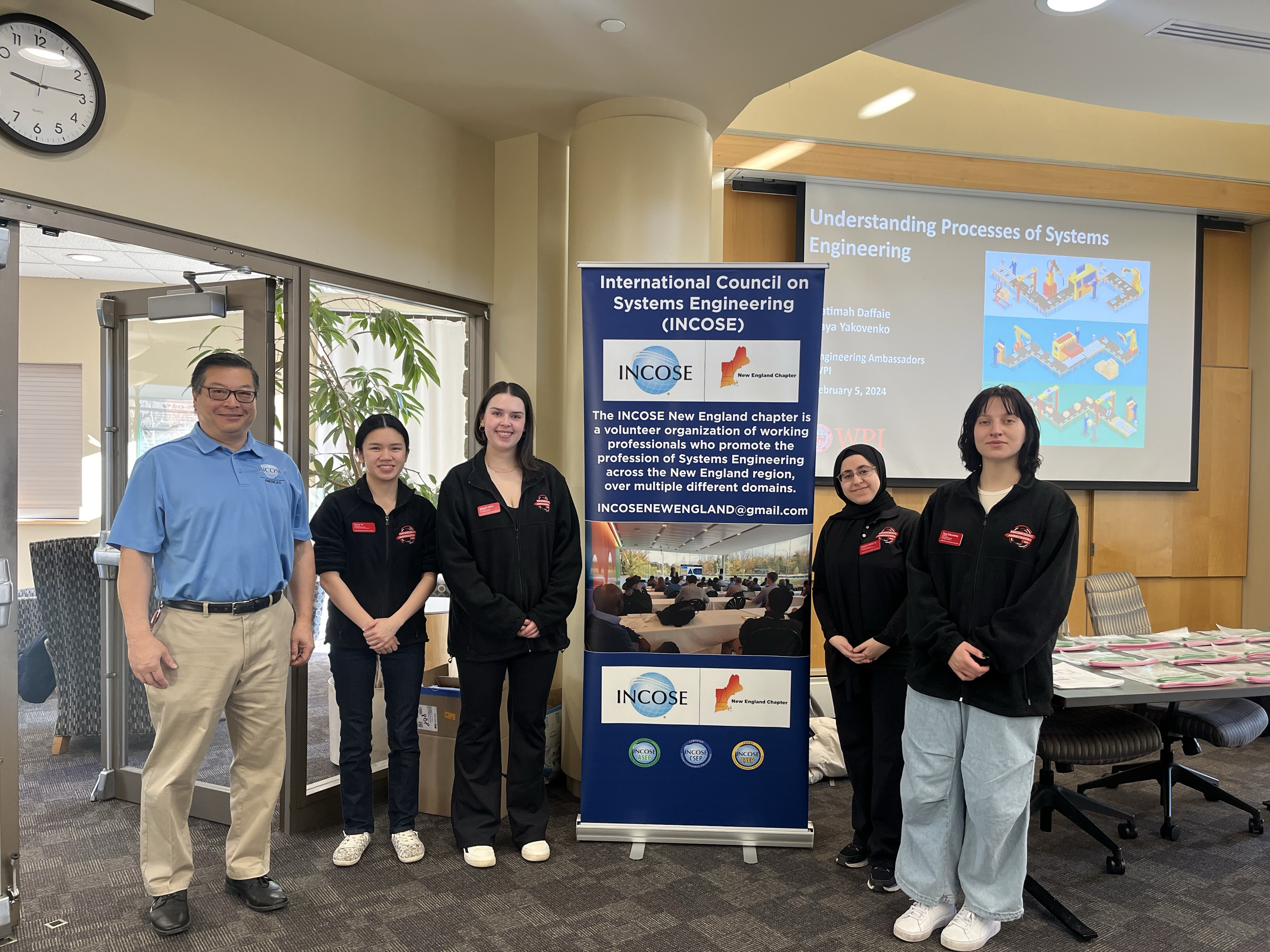 Engineering Ambassadors standing in front of sponsor banner for special systems engineering presentation