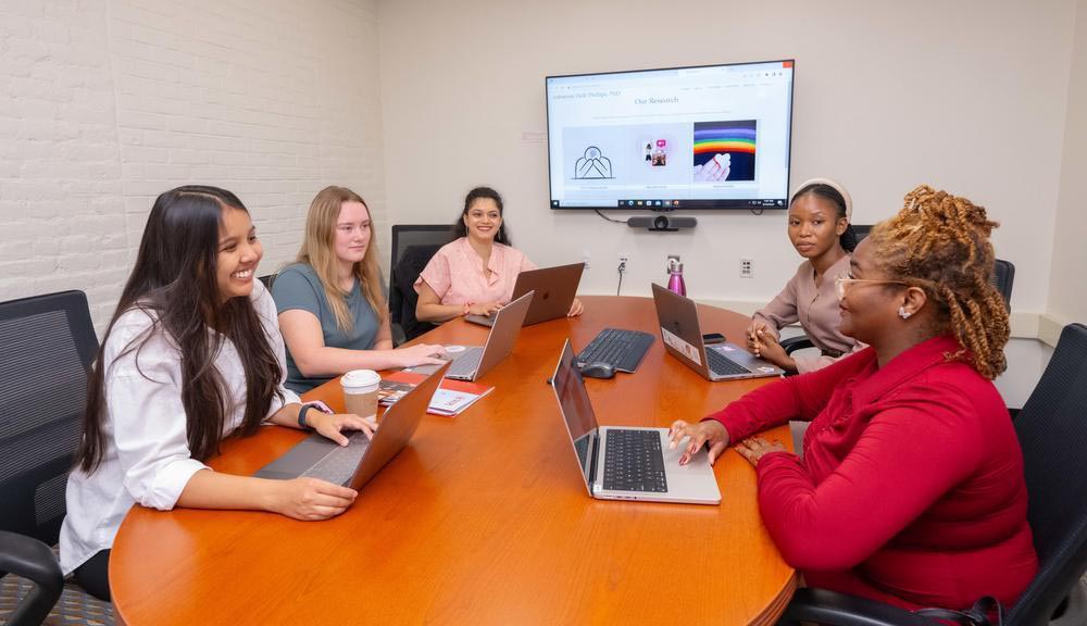 Students discuss their research work around a table.