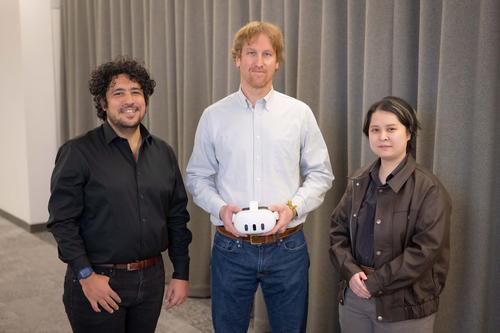 Three researchers standing together in front of a gray drape. Professor Yunus Telliel on the left wearing a black shirt, Professor Robert Dempski in the middle wearing a white shirt, PhD student Max Chen on the right wearing a brown jacket.