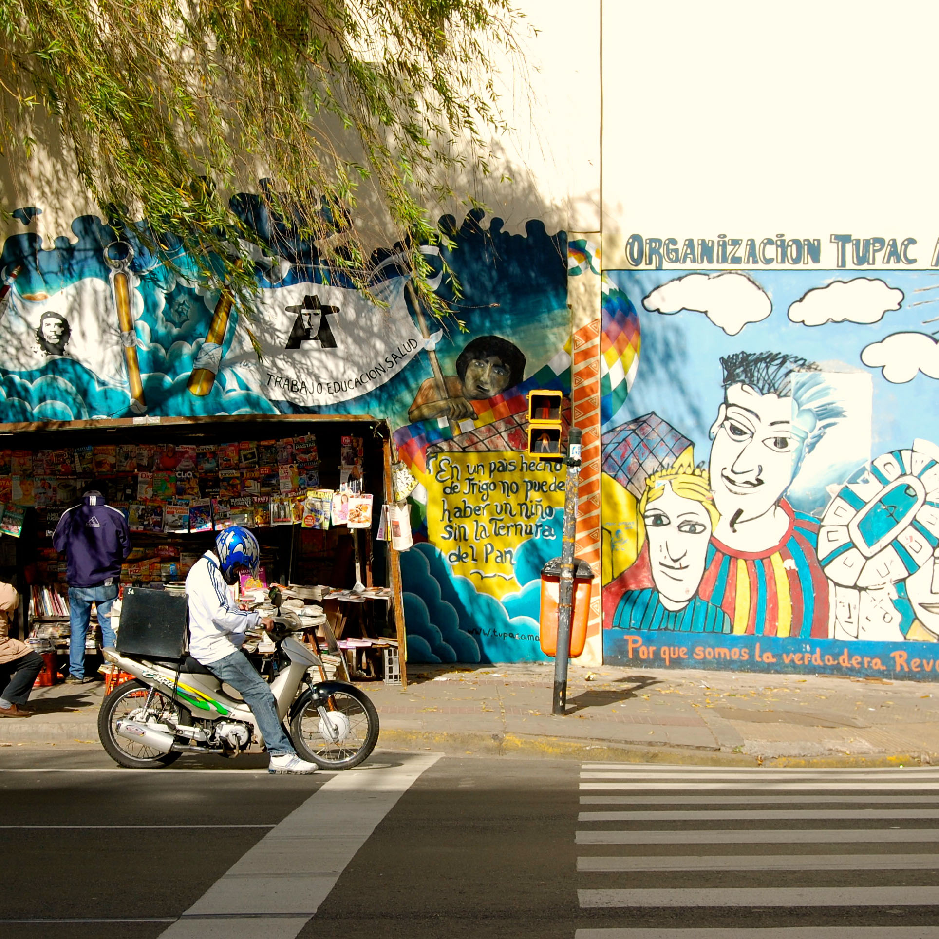 street scene with green trees and a colorful mural on a white wall
