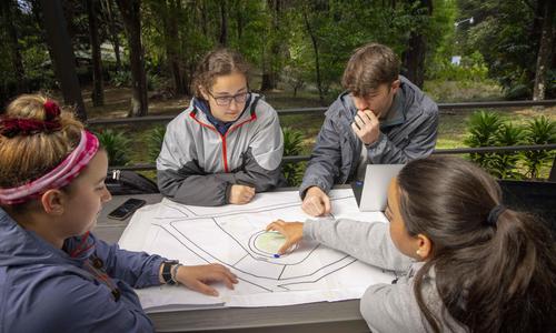 Four students look at and discuss a blueprint for a garden design