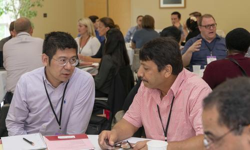 two men wearing lanyards talk during a conference work session