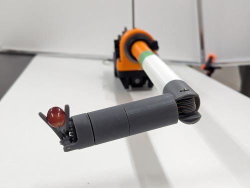 robotic surgical instrument seen in the lab. a grape is gripped by the forceps at the end of the surgical tool