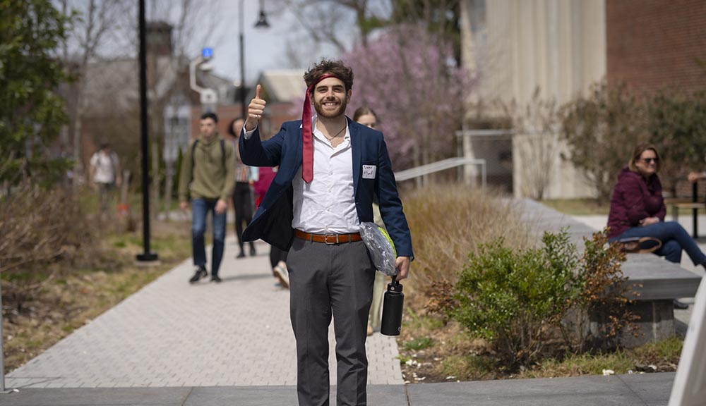 A student flashes a thumbs up with a tie around his head on campus.