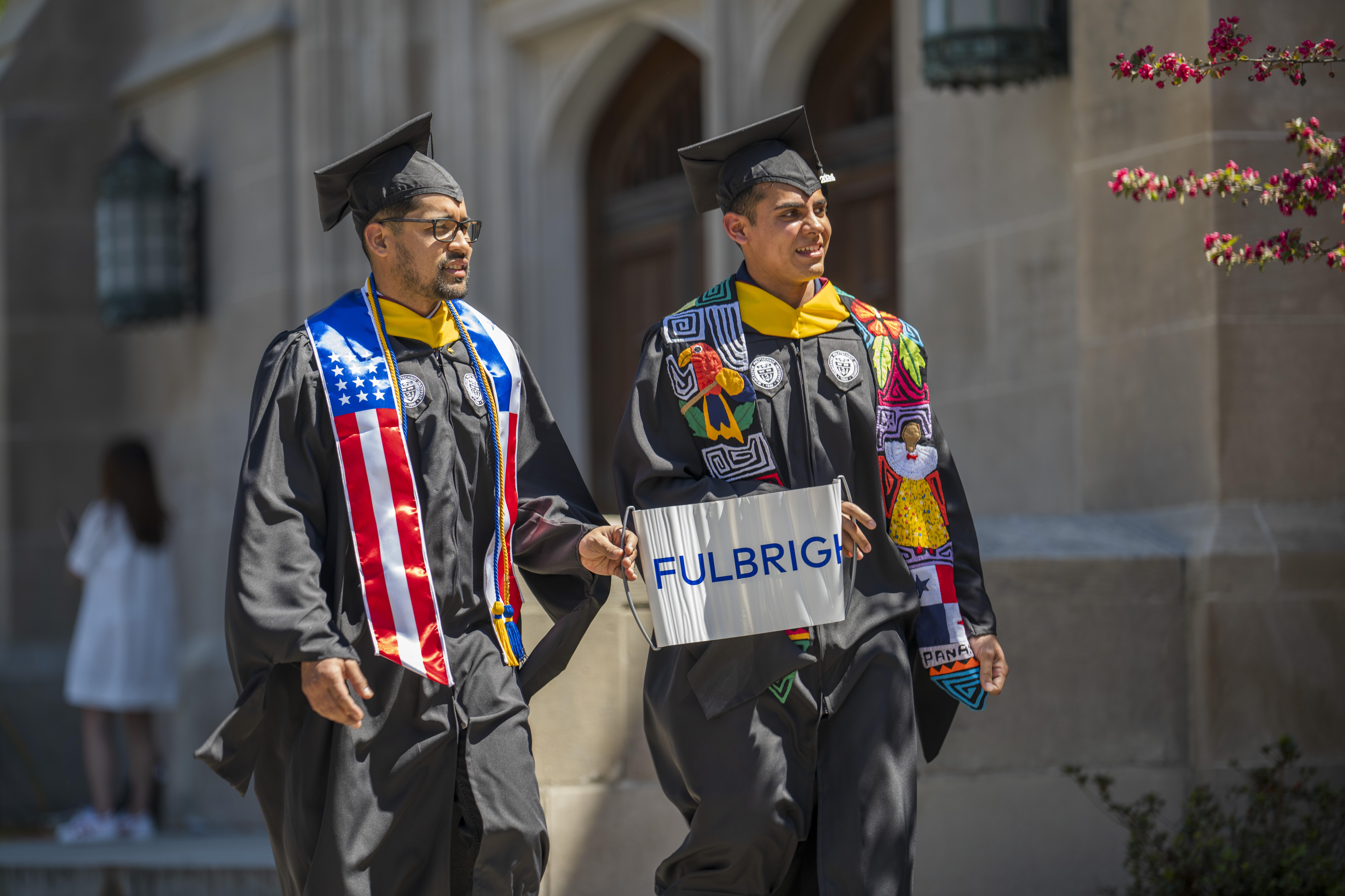WPI Fulbright Scholars in academic regalia walking and holding a banner that says, "Fulbright"