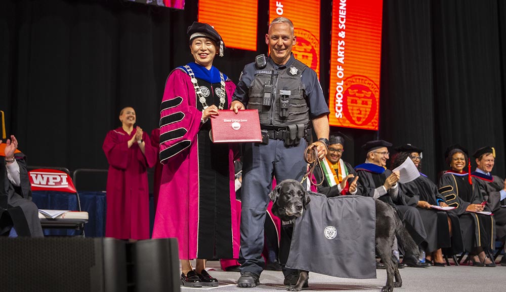 Bella and Officer Lavallee accept Bella’s diploma from President Wang onstage at Commencement.