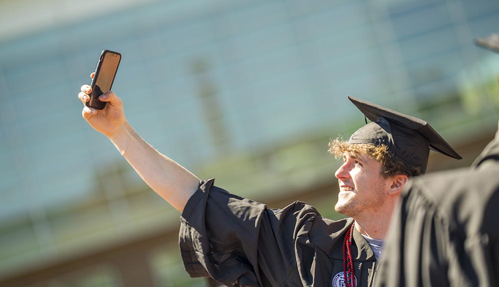 A graduate holds up their cell phone to take a selfie during the bridge crossing ceremony.