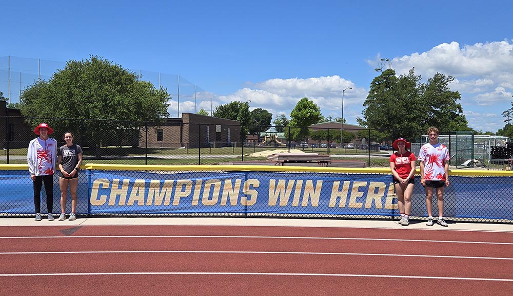 Two student athletes stand on either side of a banner reading "Champions Win Here."