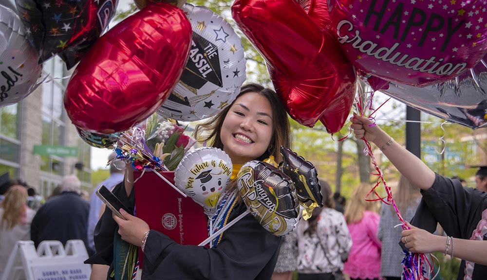 A graduate smiles with balloons around her.