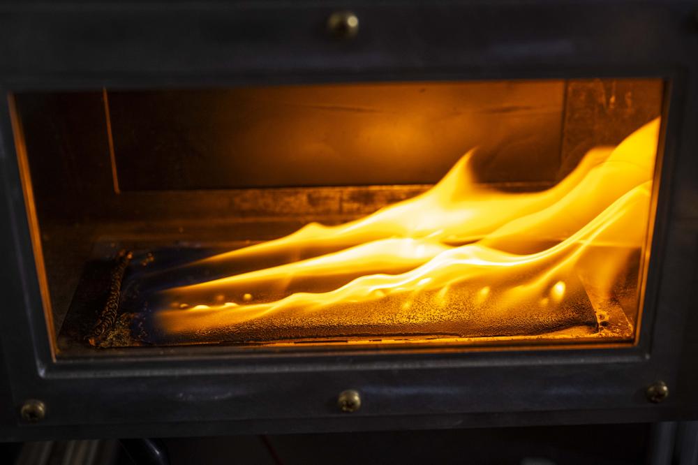A plastic fuel sample burns inside a sealed wind tunnel inside a WPI fire protection engineering research lab, as orange flames rise from the thin fuel sample 