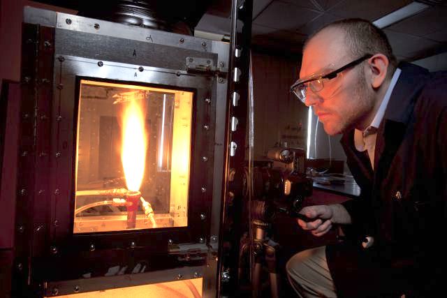 A man with protective goggles studies a bright flame in a controlled laboratory