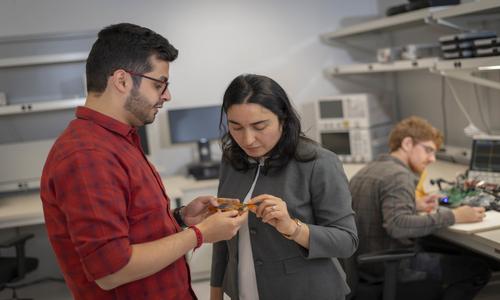 a female and male looking at equipment with a male in the background at a computer station