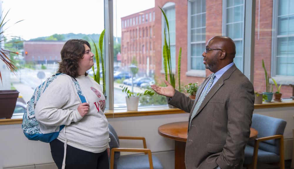 A WPI Graduate student wearing a backpack speaks to a Student Success manager dressed in a tie and jacket