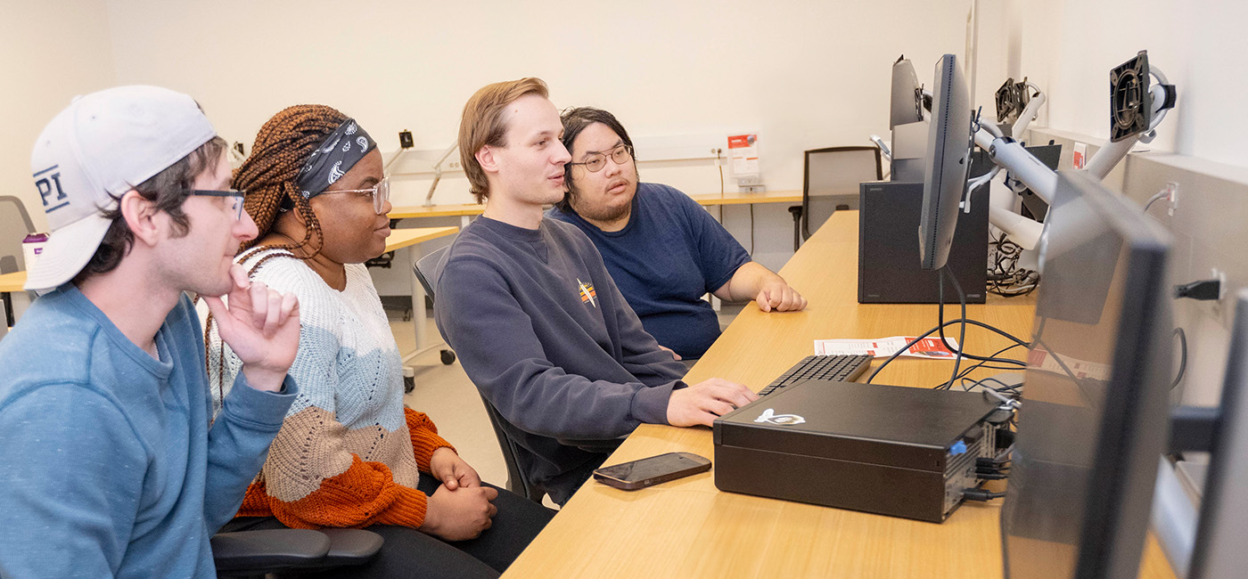 4 wpi students working together at a computer desk