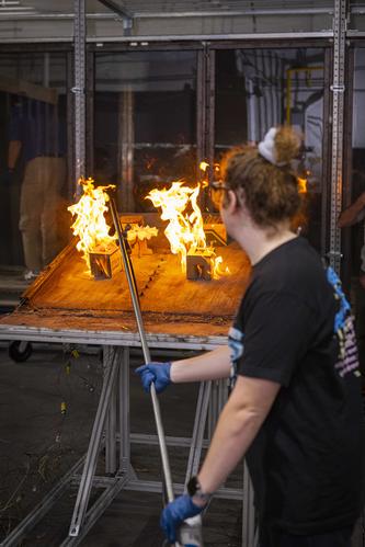 Student sets fire to cardboard model houses on a burn table in a fire laboratory during an experiment