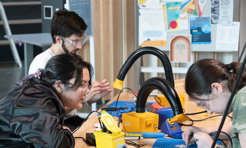 three students working on a project with tools at a table