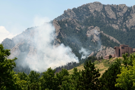 Wildfire burns in mountainous terrain not far from a building.