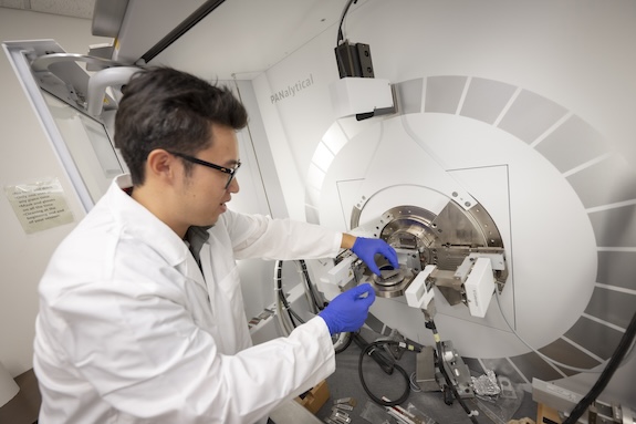 WPI student in a white lab coat uses high-tech equipment in a materials science lab