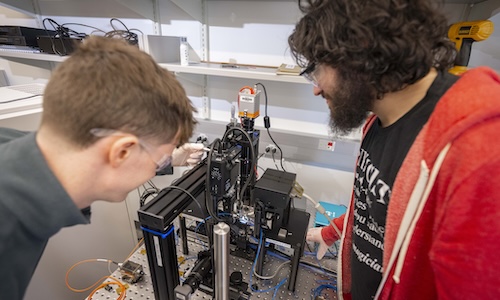 Two WPI students collaborate on a piece of technology in a photonics lab