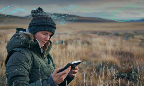 A researcher surveys a remote, rural location while using a mobile device. The head of WPI’s Social Sciences and Policy Studies department is using AI to find solutions for economic development in such locations.