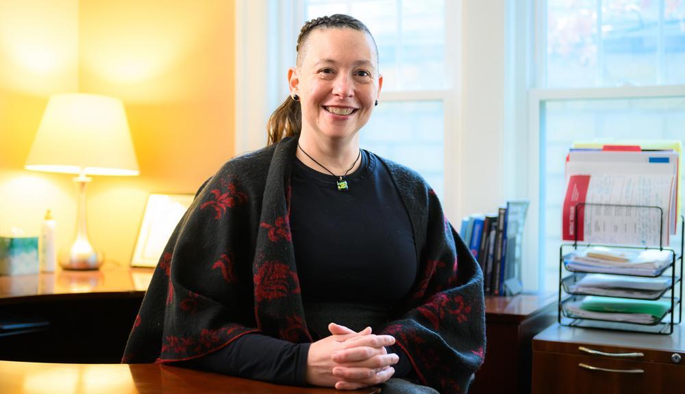 Jessi Hill sitting at desk smiling, with hands folded