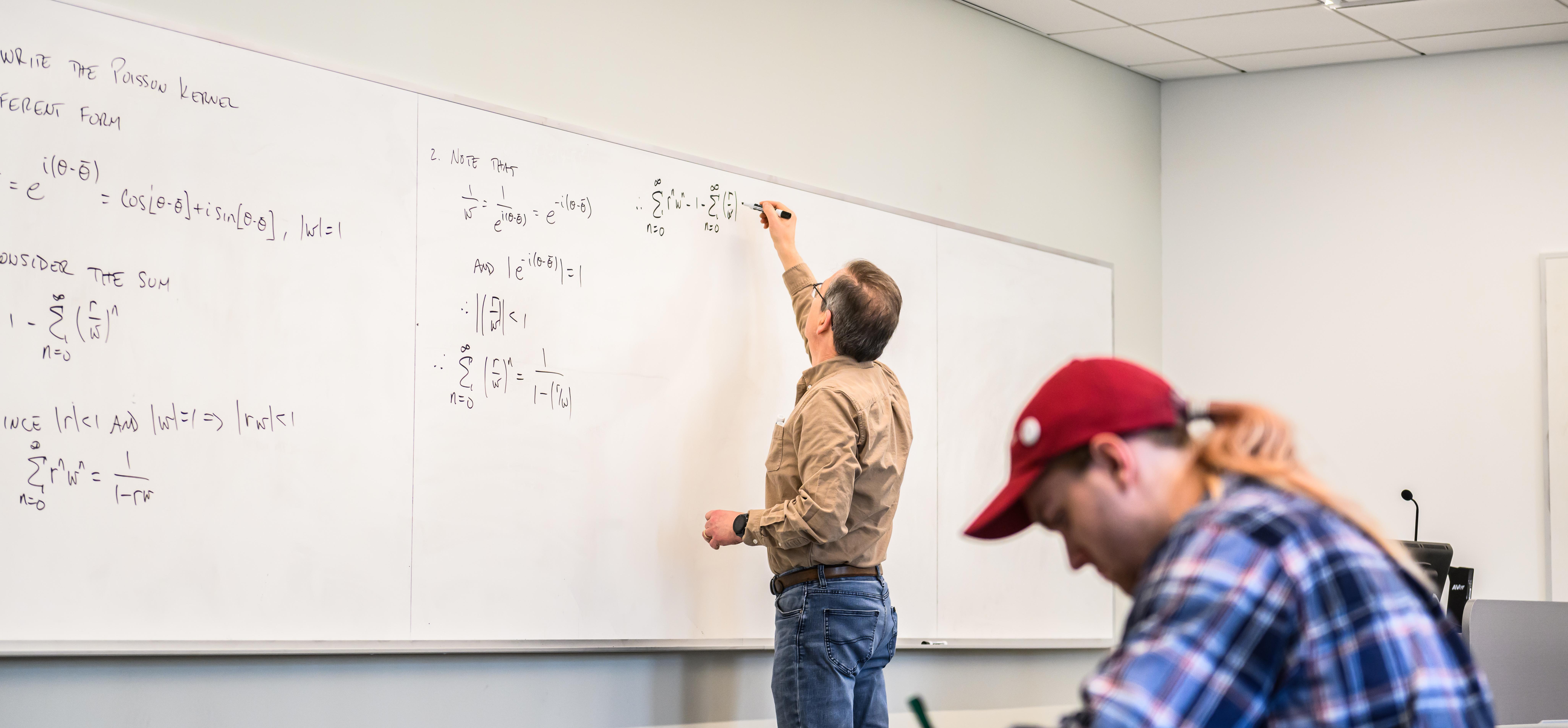 Professor at front of classroom writing on Whiteboard