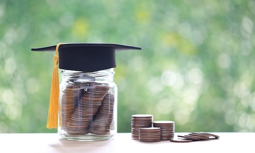 A glass jar full of coins with a square graduation cap on top