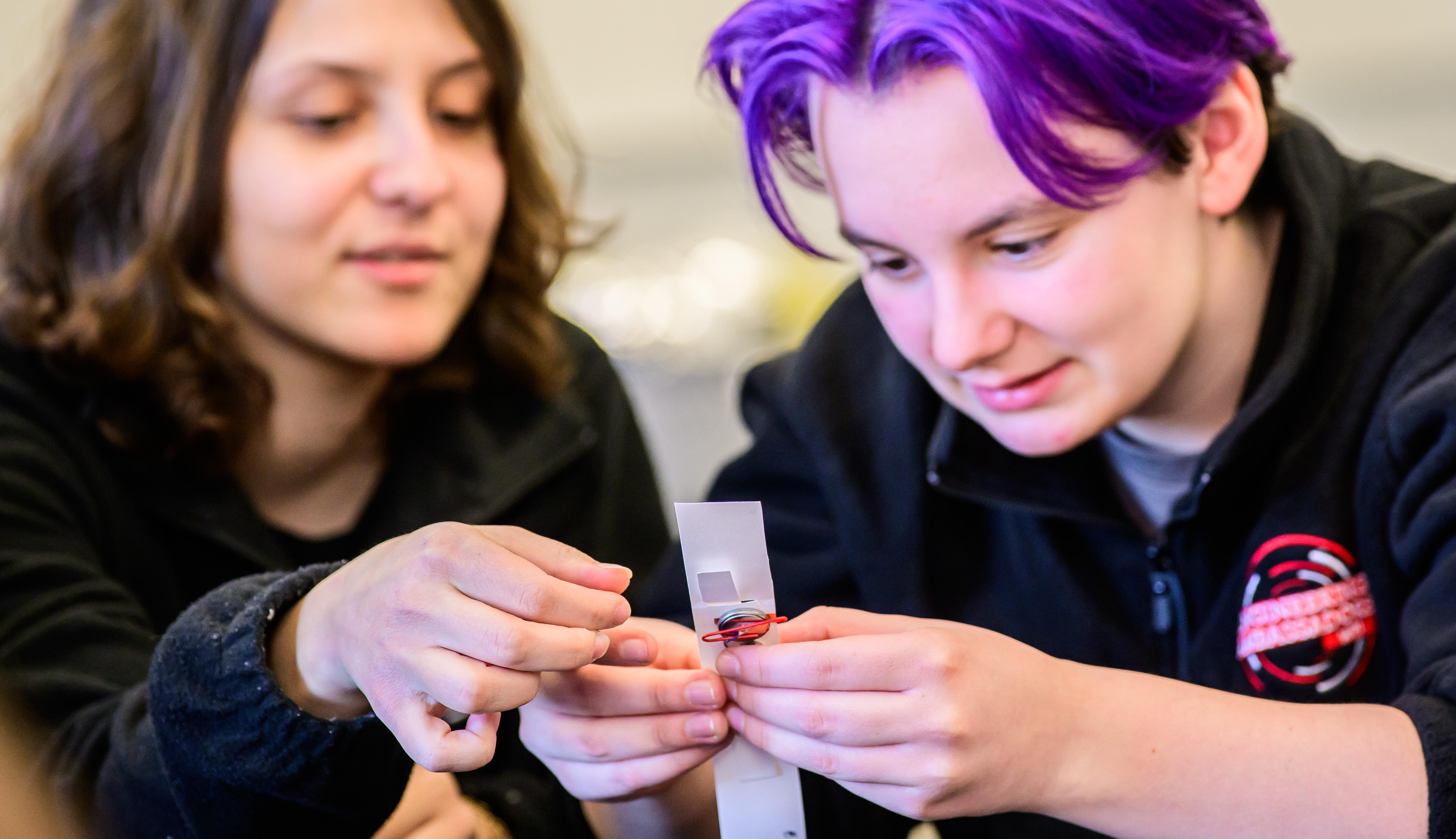 Two students collaborate to build a mechanical wristband