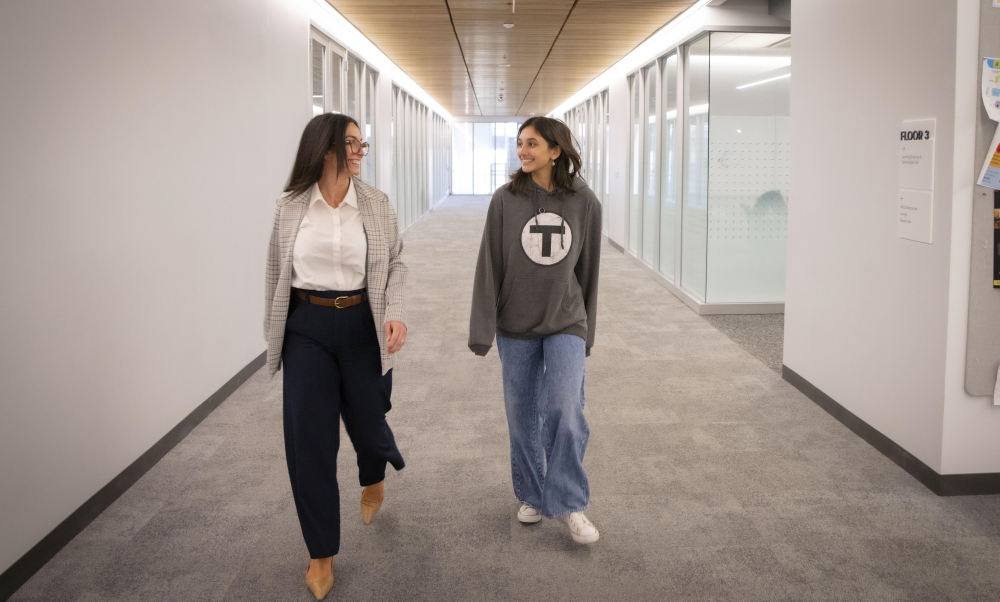 Two women, a student and her mentor, walk down a hallway smiling.