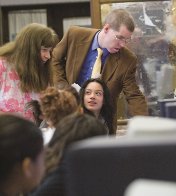 Neil Heffernan, standing, helps a student at a computer in a school classroom. The student is looking at her teacher, who is standing to the left of Heffernan.