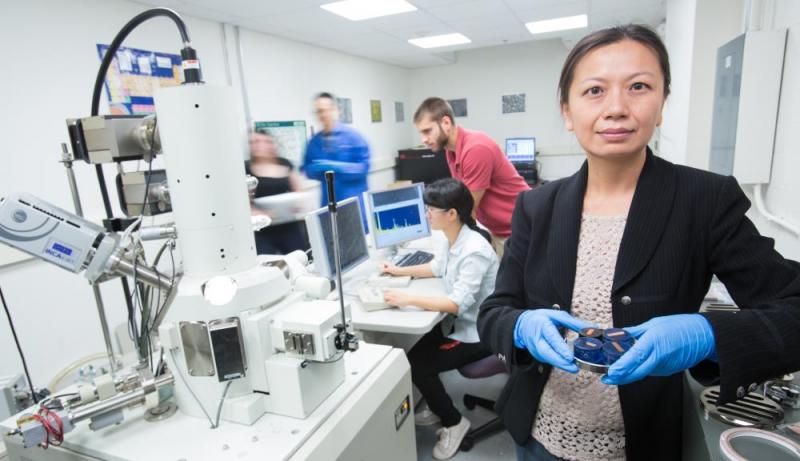 Jianyu Liang stands in the transmission electron microscope room holding a sample ready to be examined.