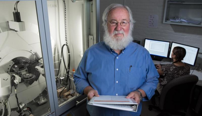 Richard Sisson, beside an x-ray diffraction instrument, faces the camera and holds a white binder